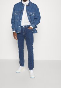 Denim jacket with button front, blue jeans, and white striped shirt, paired with white sneakers featuring light blue accents.