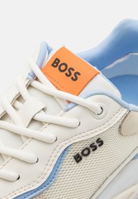 Baskets blanches et bleu clair avec lacets blancs, étiquette orange sur la languette et logo « BOSS » sur le panneau latéral en mesh et l’étiquette de la languette.