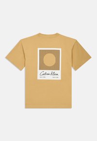 Κοντομάνικο μπλουζάκι μουστάρδι με γραφικό στην πλάτη που έχει άσπρη ορθογώνια περιφέρεια, κατακόρυφες γραμμές και έναν κεντρικό κύκλο. Περιλαμβάνει το λογότυπο Calvin Klein.