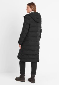 Black puffer coat with a hood, featuring a long design and quilted texture. Worn with dark pants and brown ankle boots.