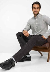 Camicia grigia a maniche lunghe con un motivo sottile, abbinata a pantaloni grigio scuro e scarpe in pelle nera con fibbia, seduto su una sedia di legno.