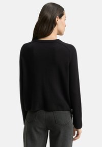 Zwarte trui met een gestructureerde afwerking, geribbelde halslijn en lange mouwen, gecombineerd met donkergrijze high-waisted jeans met achterzakken.
