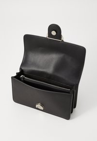 Sac en cuir noir au design épuré, avec une fermeture à pression en argent, une poche intérieure zippée et une texture lisse.