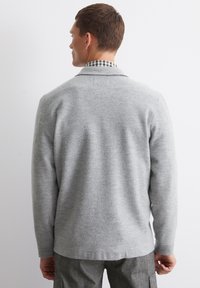 Gray wool sweater with long sleeves and a relaxed fit. Features a subtle texture and a rounded hem. Layered over a checkered shirt.
