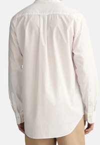 Bílá košile s dlouhým rukávem, s rozparkem vzadu, rovný lem a manžety na knoflíky. Vyrobena z texturované tkaniny. Jednoduchý, minimalistický design.