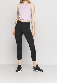 Top sportivo lilla annodato in vita, abbinato a leggings neri a vita alta e scarpe sportive nere con dettagli bianchi.