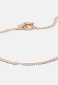 Pulsera en tono dorado con una cadena de metal flexible y texturizada, equipada con un cierre de toggle, que muestra un diseño elegante y minimalista.