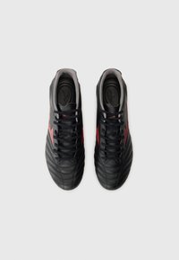 Black leather soccer shoes feature a textured design with red accents, rounded toe, and black laces on a gray lining.