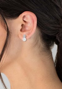 Pendientes de perlas en forma de gota con un acento de cristal en la parte superior. La parte superior es redonda con una textura brillante, mientras que la parte inferior presenta una perla lisa y brillante.