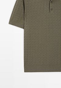 Olijfgroene gebreide poloshirt met een gestructureerd kabelpatroon, korte mouwen en een klassieke kraag. Drie knopen bij de hals.