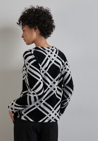 Svart och grå tröja med geometriskt mönster, med en mjuk textur, rund halsringning och långa ärmar. Stiliserad med avslappnad passform.