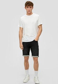 T-shirt en coton blanc associé à un short en denim foncé. Le short présente des ourlets retroussés, porté avec des baskets montantes blanches et des chaussettes blanches.