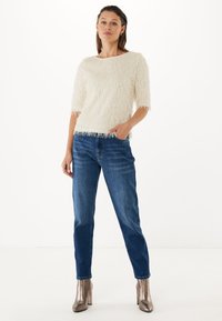 Maglione bianco con frange, dalla scollatura ampia, abbinato a jeans dritti blu scuro e stivali con tacco alto metallici.