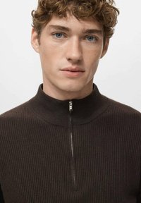 Suéter marrón acanalado con cuello alto y cremallera al cuarto. La textura de la tela parece suave con un detalle de cremallera lisa en el cuello.