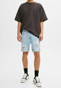 T-shirt noir surdimensionné, shorts en denim bleu clair avec des bords effilochés, manches roulées, et baskets montantes noires avec des accents blancs et des lacets.