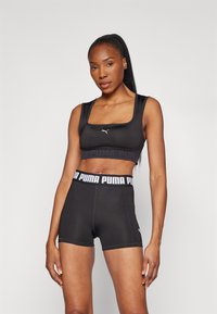 Top corto atlético negro y pantalones cortos de tejido suave. El top presenta un escote cuadrado y un logotipo, mientras que los pantalones cortos tienen una cinturilla con marca.
