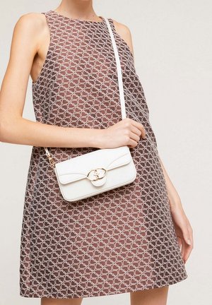 Brązowa sukienka bez rękawów z białym wzorem, noszona przez osobę trzymającą małą białą torebkę na ramię z złotą klamrą.
