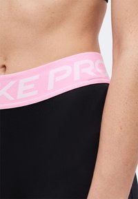 Gros plan sur la taille d’une personne portant une tenue de sport noire avec une ceinture rose portant l’inscription « NIKE PRO ».