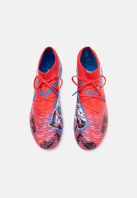 Scarpe da ginnastica rosse e blu con una superficie texturizzata, caratterizzate da un upper in maglia, motivi intricati e lacci in contrasto.