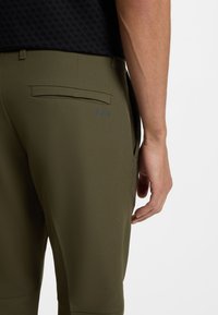 Spodnie w oliwkowej zieleni o gładkiej fakturze, wyposażone w tylną kieszeń oraz subtelne logo „BOSS”. Pas jest gładki, a szwy starannie wykończone.