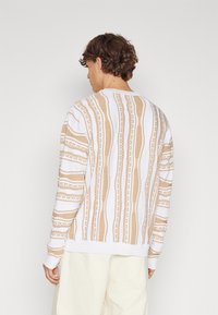 Beige- och vita randiga tröja med texturerade mönster, ribbad rundhalsad och muddar, tillverkad av mjukt stickat tyg.