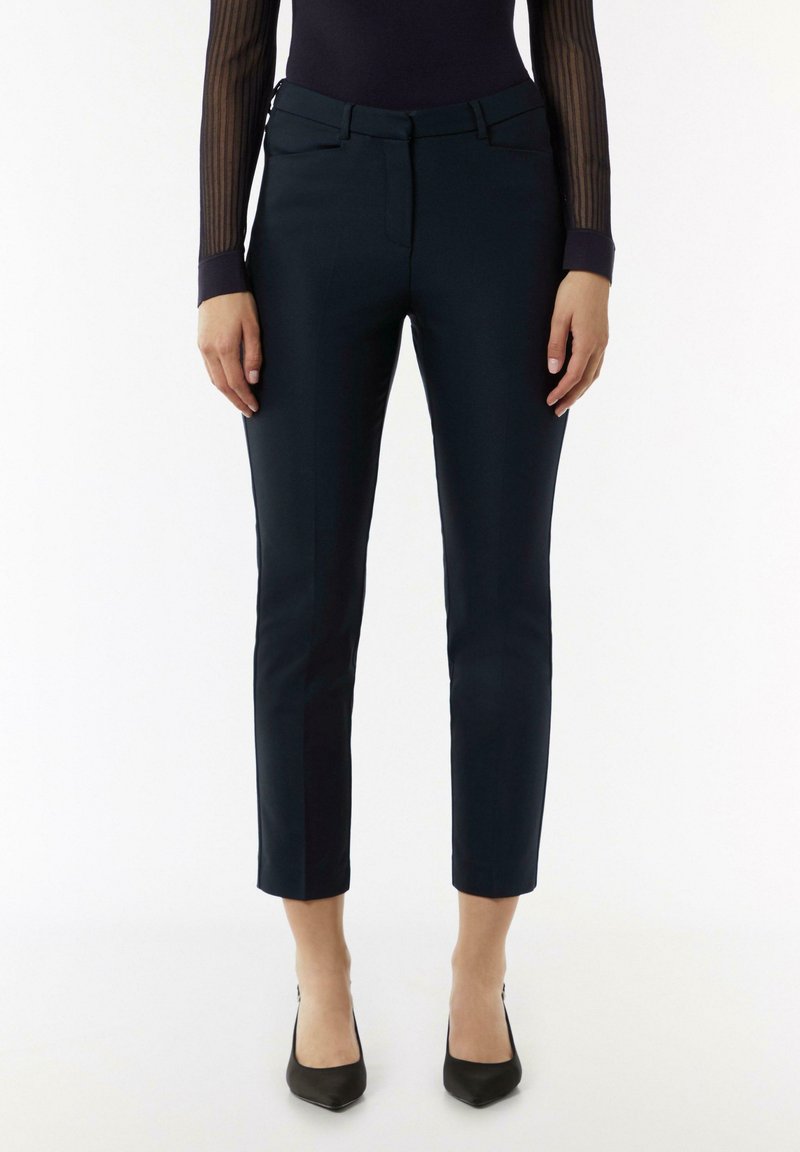 Marineblauwe tailored broek met een slim fit, cropped lengte, steekzakken en riemlussen. De stof lijkt glad en licht elastisch.