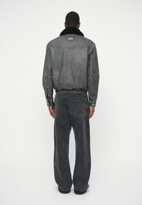 Veste en denim noir avec un col en fourrure, présentant un design court, des coutures visibles, et un jean noir ample avec une texture subtile.