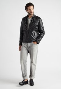 Sort læderjakke med ståkrave, front lynlås og to lynlåsede lommer. Båret med lysegrå, let tilspidsede jeans og sorte loafers.