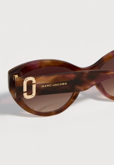 Γυαλιά ηλίου Marc Jacobs σε σχέδιο χελώνας με οβάλ φακούς και χρυσή λεπτομέρεια λογότυπου στο πλαϊνό μέρος.
