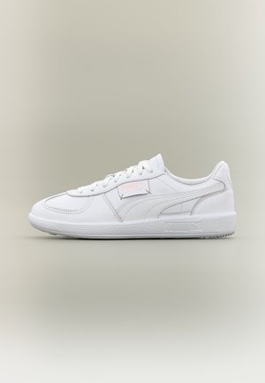 White low-top Puma sneaker with lace-up closure, subtle branding on the side and tongue, on a neutral beige background.