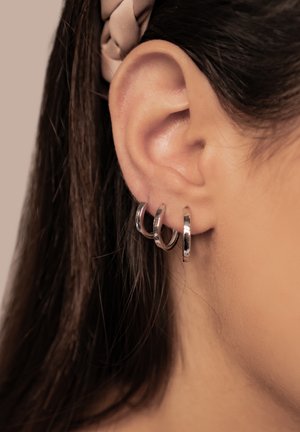 Silberne Creolen mit drei gestapelten Ringen, die eine glatte, polierte Oberfläche und eine kreisförmige Form aufweisen, getragen in einem durchstochenen Ohrläppchen.