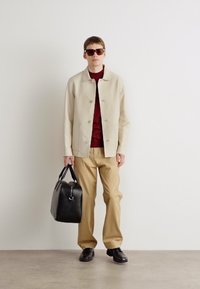 Beige lightweight jacket with round buttons, maroon turtleneck, beige trousers, black leather bag, and sunglasses. Smooth texture, casual fit.