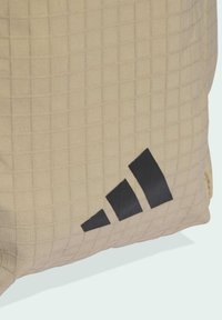 Beige quilted bag with a textured surface. Features a prominent black Adidas logo on the side. Durable material with a sleek design.