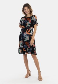 Rochie neagră cu modele florale și de frunze vibrante în roșu, portocaliu și verde. Mâneci scurte cu volănașe și o curea de legare la talie.