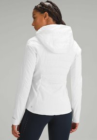 Veste blanche légère avec capuche, dotée d'une finition texturée et de ventilations latérales. Coupe slim avec des manches longues et un détail de logo sur le poignet.