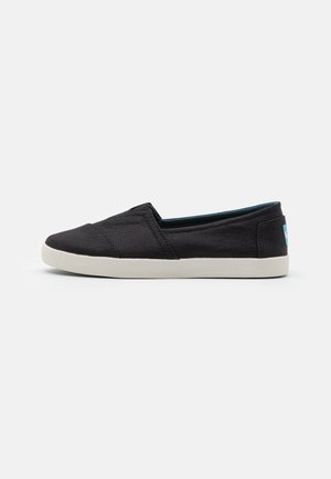 Sort slip-on lærreds fritidssko med hvid sål, lav profil og blå label på hælen, vist fra ydersiden på en ensfarvet baggrund.