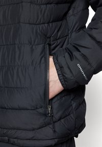 Giacca a vento nera con trapuntatura orizzontale, tasca con zip e marchio "OMNI-HEAT" sul polsino. Il materiale appare liscio e texturizzato.
