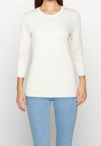 Leicht gestreiftes Langarmoberteil in Creme und Beige mit einem Rundhalsausschnitt, aus weichem Stoff, kombiniert mit engen blauen Jeans.