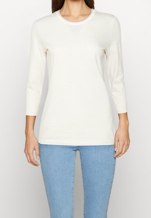 Leicht gestreiftes Langarmoberteil in Creme und Beige mit einem Rundhalsausschnitt, aus weichem Stoff, kombiniert mit engen blauen Jeans.