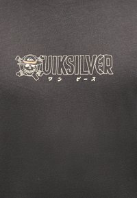 Κρανίο που φοράει καπέλο με σταυρωμένα οστά δίπλα σε έντονο κείμενο "QUIKSILVER" και ιαπωνικούς χαρακτήρες πάνω σε σκούρο υφασμάτινο φόντο.