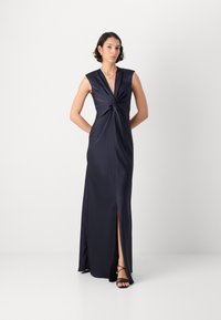 Navy satiini mekko, jossa on syvä kaula-aukko, solmittu etudetalji ja sivuaukko. Varustettu hihattomilla hihoilla ja sileällä, tyylikkäällä muotoilulla.