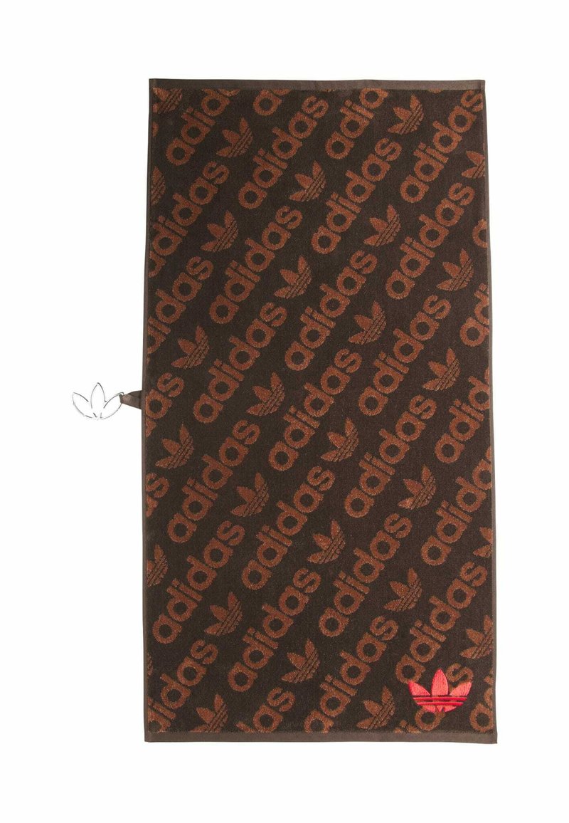 Braunes Handtuch mit einem Allover-Muster des Schriftzugs "adidas" und Logo, mit rotem Logoakzent in einer Ecke. Weiche Textur.