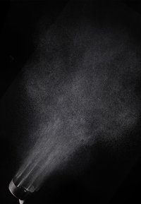 Sprayfles die een fijne nevel verspreidt, met een doorzichtig kunststof lichaam en een zwarte spuitmond. De nevel lijkt delicaat tegen een donkere achtergrond.