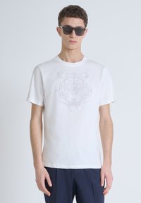 Camiseta blanca de algodón con un gráfico tonal de tigre en el frente. La camiseta tiene un escote redondo y mangas cortas. Diseño minimalista.