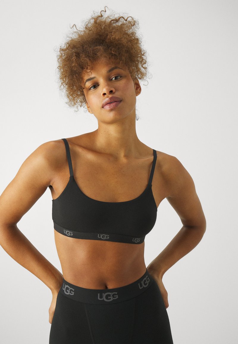 Svart sømløs bralette med tynne stropper, UGG-logo på båndet, som har en elegant, avrundet utringning og myk tekstur.