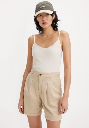 Shorts plissés beige taille haute avec une fermeture à bouton, associés à un débardeur blanc ajusté en côte avec des bretelles spaghetti.