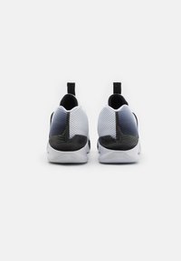 Trainingsschuhe mit einem schwarz-weißen Farbverlauf, gerippter Textur, abgerundeter Form und Zuglasche an der Ferse für einfaches An- und Ausziehen.