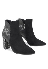 Botas de tobillo negras de ante con punta afilada, que presentan un patrón de serpiente negra y plateada texturizado en el tacón y detalle de cremallera lateral.