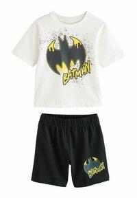 Vit bomull t-shirt med svart och gul Batman-logotyp samt stänkmönster, i kombination med svarta bomullsshorts som har en gul logotypaccent.