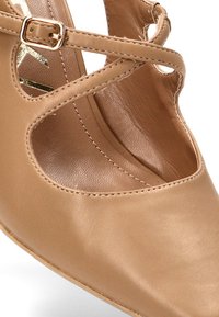 Zapato de tacón de piel beige con tiras entrecruzadas, cortes abiertos y una textura suave. Punta afilada y detalles de costura sutiles.